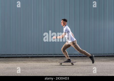 Giovane uomo skateboard di fronte al muro Foto Stock