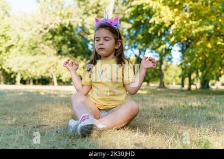 Ragazza che pratica yoga seduto sull'erba al parco Foto Stock