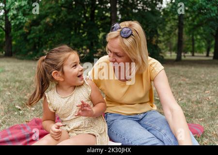 Ragazza felice con nonna seduta su coperta da picnic al parco Foto Stock