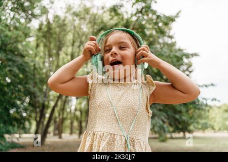 Ragazza felice che ascolta la musica attraverso le cuffie al parco Foto Stock