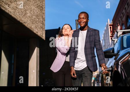 Giovane donna appoggiata all'uomo che carica l'auto elettrica Foto Stock
