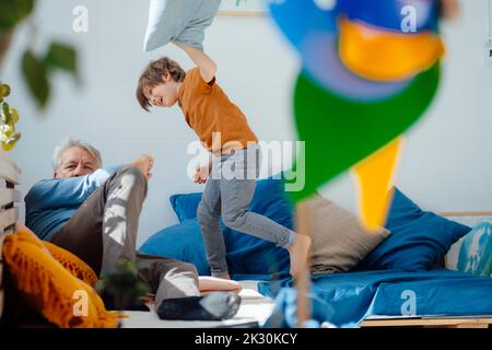 Buon nipote che gioca a cuscino lotta con nonno in salotto Foto Stock