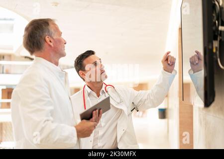 Il medico spiega il collega attraverso lo schermo sulla parete in ospedale Foto Stock