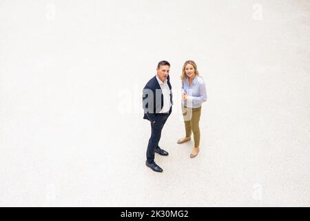 Uomo d'affari con mano in tasca in piedi con donna d'affari in ufficio Foto Stock