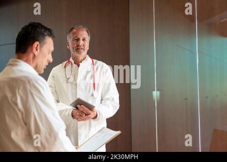 Medico senior che tiene un tablet PC con un collega che esamina il rapporto in ospedale Foto Stock