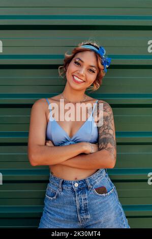 Giovane donna felice con le braccia incrociate in piedi davanti al muro verde Foto Stock