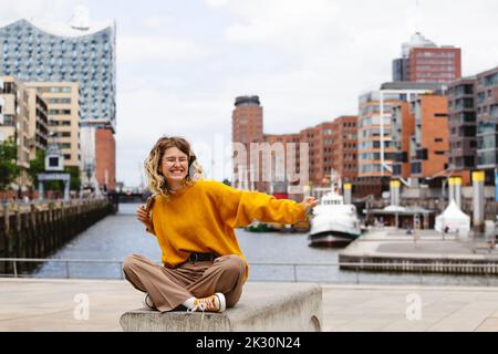 Felice giovane donna che allunga le braccia a Elbphilharmonie Foto Stock