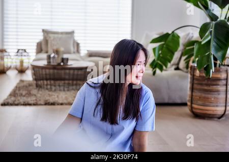 Donna matura sorridente seduta sul pavimento a casa Foto Stock