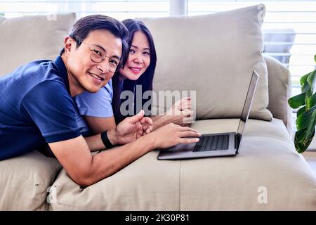 Felice coppia matura con il notebook sdraiato sul divano a casa Foto Stock