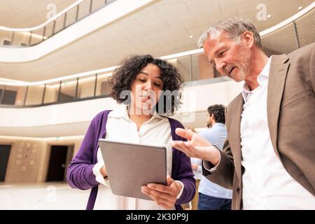 Colleghi aziendali multirazziali che discutono su un tablet in corridoio Foto Stock