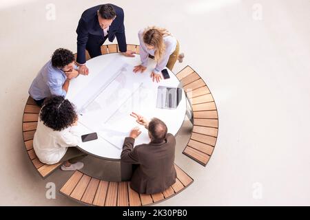 Colleghi di affari multirazziali che discutono sopra documento sul tavolo in corridoio Foto Stock