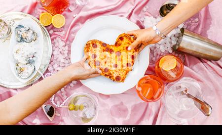 Mano delle donne che tirano la pizza a forma di cuore a tavola Foto Stock