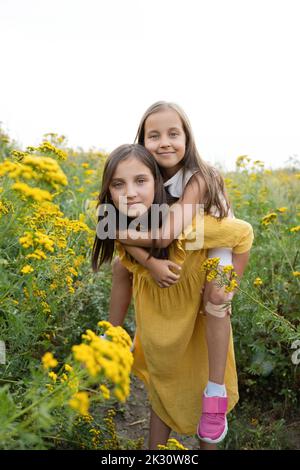 Ragazza che dà cavalcata piggyback a sorella in campo Foto Stock