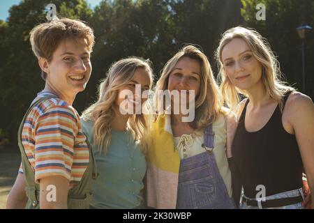 Felice persona non binaria con gli amici in piedi al parco nella giornata di sole Foto Stock