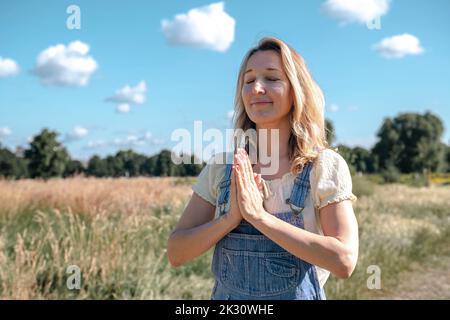 Donna matura sorridente con le mani afferrata in preghiera il giorno di sole Foto Stock