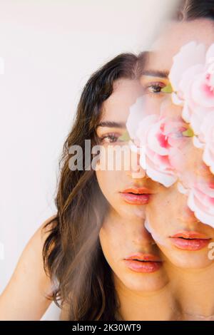 Esposizione multipla della donna che tiene il fiore rosa sopra l'occhio Foto Stock