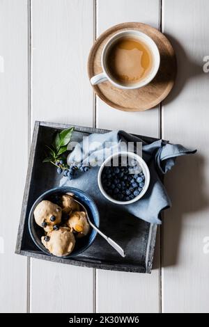 Tazza di caffè e ciotola di gelato fatto in casa alle arachidi con mirtilli Foto Stock