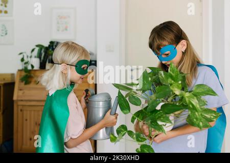 Le ragazze in costume di superdonna che tiene in vaso la pianta e l'annaffiatura possono nel paese Foto Stock