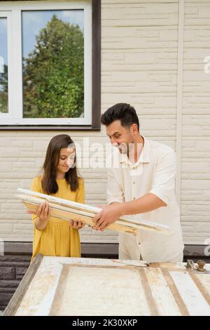 Ragazza sorridente aiutare padre ripristinare porta nel cortile posteriore Foto Stock