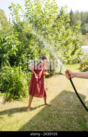 Ragazza che gioca con l'acqua attraverso il tubo flessibile in giardino il giorno di sole Foto Stock