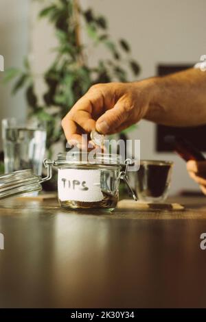 Mano dell'uomo d'affari che mette la moneta nel vaso della punta alla caffetteria Foto Stock