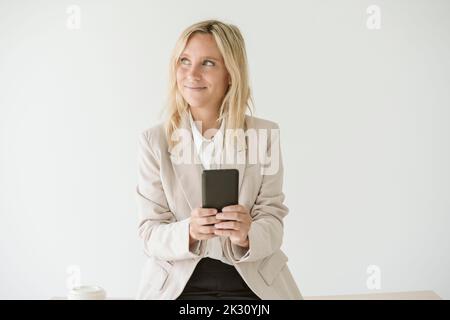 Donna d'affari che usa il telefono cellulare che guarda lontano Foto Stock