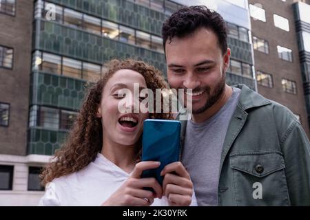 Donna felice che condivide lo smartphone con un amico di fronte all'edificio Foto Stock