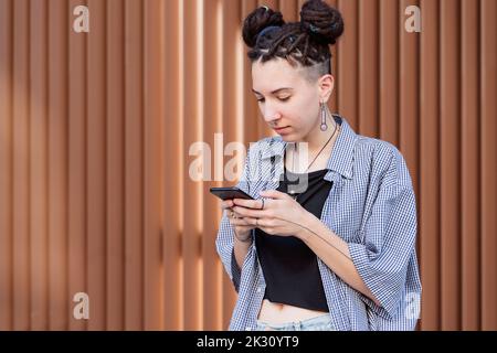 Persona non binaria che utilizza lo smartphone davanti alla parete Foto Stock