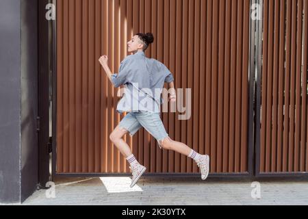 Persona non binaria che corre davanti al muro Foto Stock