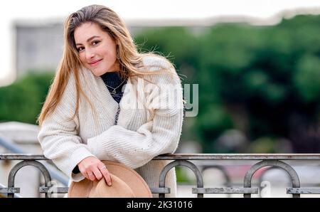 Donna sorridente che indossa un maglione appoggiato sulla ringhiera Foto Stock