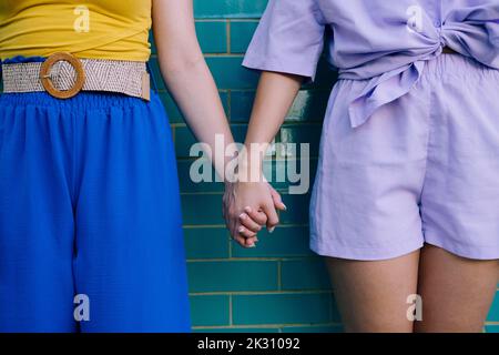 Giovani donne che tengono le mani in piedi davanti al muro di mattoni Foto Stock