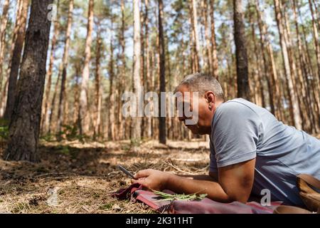 Uomo maturo che utilizza uno smartphone sdraiato nella foresta Foto Stock