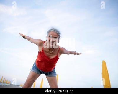 Donna anziana sorridente che fa ginnastica in spiaggia Foto Stock