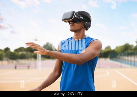 Giovane uomo che indossa gli occhiali VR che si profora in piedi in campo da basket Foto Stock