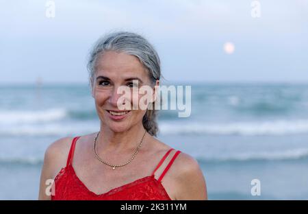 Donna anziana felice con i capelli grigi alla spiaggia Foto Stock