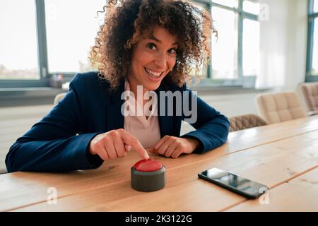Donna d'affari sorridente che tocca il pulsante del cicalino in ufficio Foto Stock