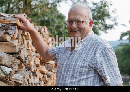 Uomo anziano sorridente da pila di legna da ardere Foto Stock