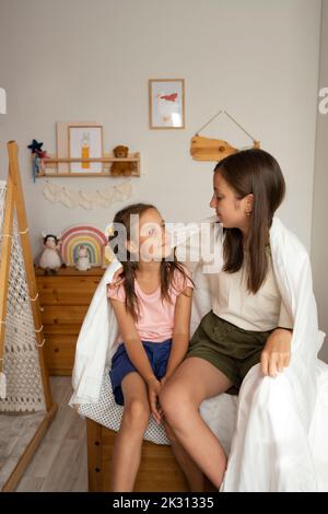 Sorelle avvolti in coperta seduta insieme sul letto Foto Stock