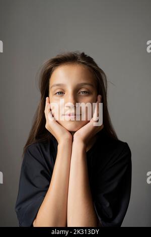 Ragazza sorridente con la testa in mano contro sfondo grigio Foto Stock