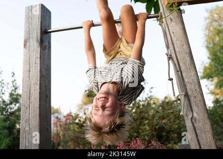 Ragazzo allegro appeso capovolto sulla barra orizzontale Foto Stock