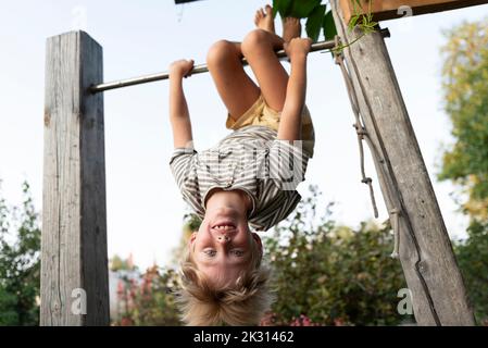 Ragazzo felice appeso capovolto sulla barra orizzontale Foto Stock