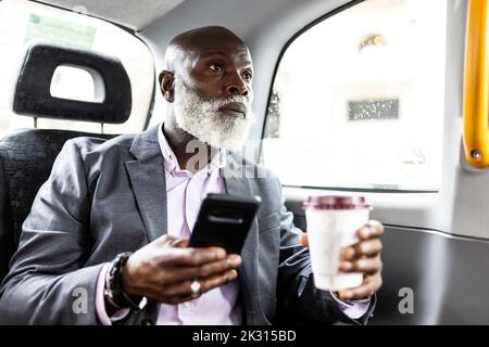 Passeggero senior con smartphone con caffè in taxi Foto Stock