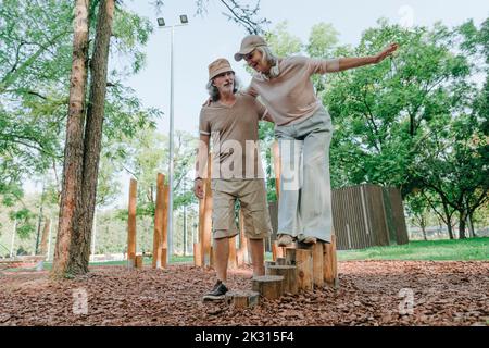 Uomo anziano che sostiene la donna che bilancia sul ceppo dell'albero nel parco Foto Stock