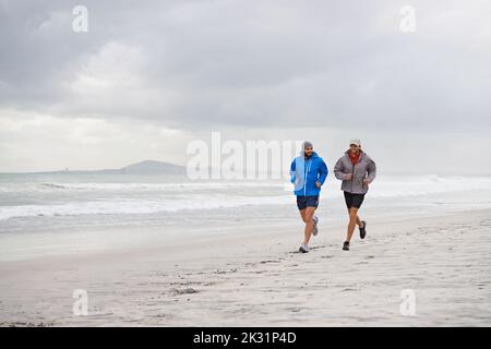 Mattina correre sulla spiaggia con un amico. Scatto a tutta lunghezza di due uomini che camminano insieme lungo la spiaggia in una mattinata piena. Foto Stock