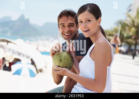 Rilassarsi in una vacanza tropicale. Giovane coppia che si gode un drink da una noce di cocco. Foto Stock