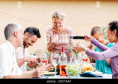 Un gruppo di amici adulti che condividono il cibo in una festa barbecue con un sacco di cibo e bevande al tavolo. Concetto di stile di vita. Foto Stock