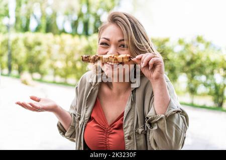 Giovane donna chubby che si diverte nel parco a barbecue facendo facce tenendo spiedini - cibo e bevande, persone, concetto di stile di vita Foto Stock