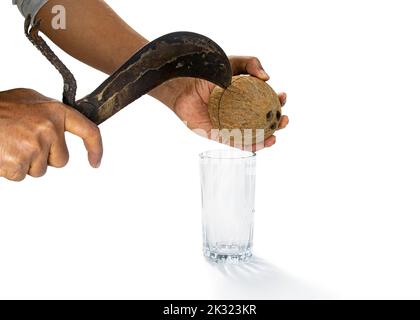 Un uomo sta rompendo una cellula di cocco con un coltello boti per ottenere l'acqua di cocco da esso. Tenendo un utensile da taglio in una mano e il cocco maturo in un'altra impugnatura. Foto Stock