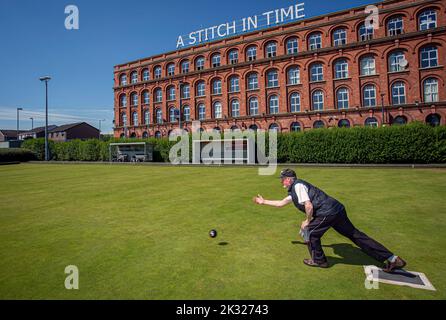 Uomo che gioca a bocce nel Brooke Park Bowling Club di fronte alla Old Rosemount Factory, Derry in Irlanda del Nord. Foto Stock