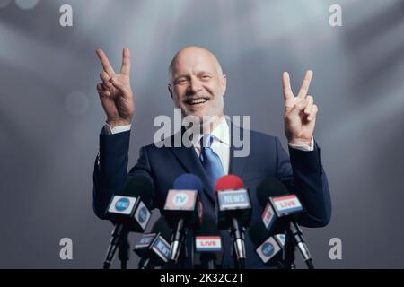 Leader fiducioso e di successo intervistato dai media, sta sorridendo e facendo un segno V. Foto Stock